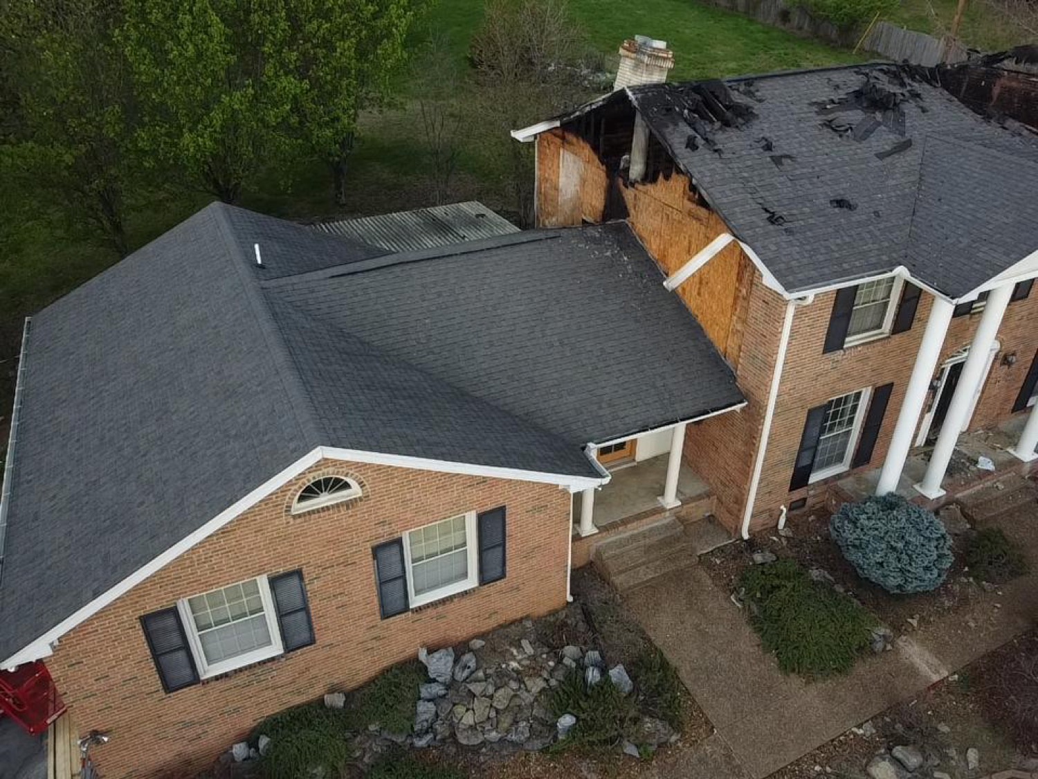 Brick colonial home with a fire-damaged, burned-open roof wing before RoofWrap