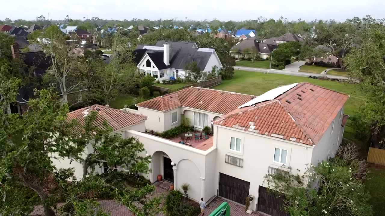 Tile roof home with its original clay tile roof, neighbor's roof under a blue tarp in the background