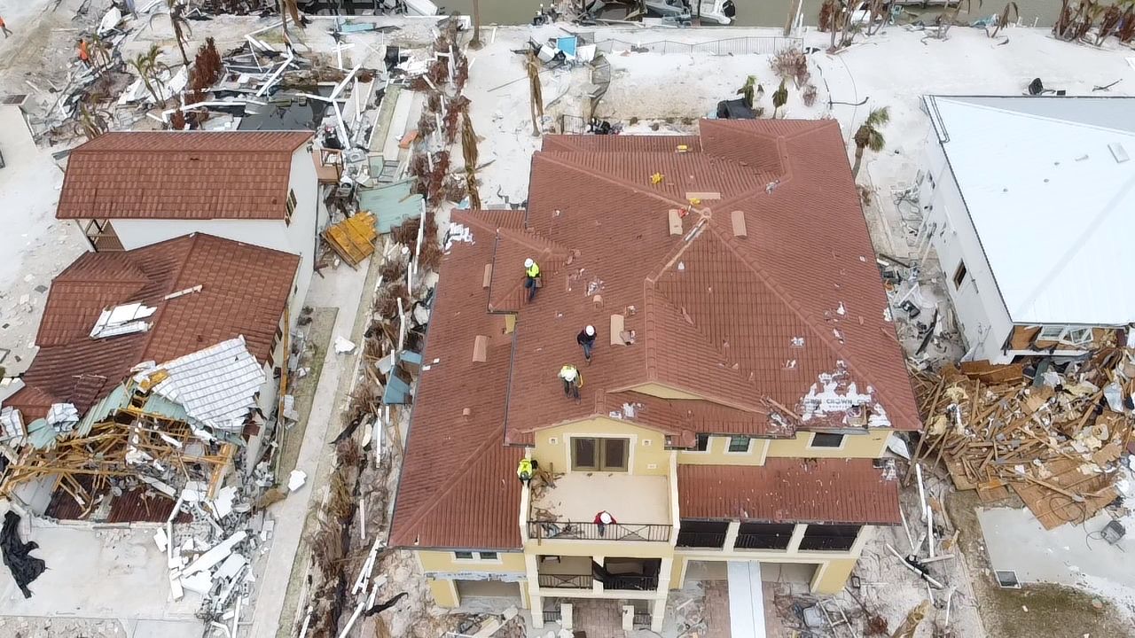 Clay tile roof home after hurricane damage, tile missing and storm debris in the yard