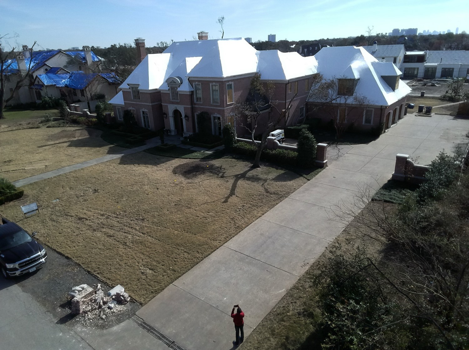 A RoofWrapped home with a clean white roof beside a neighbor still under blue tarps after the same storm