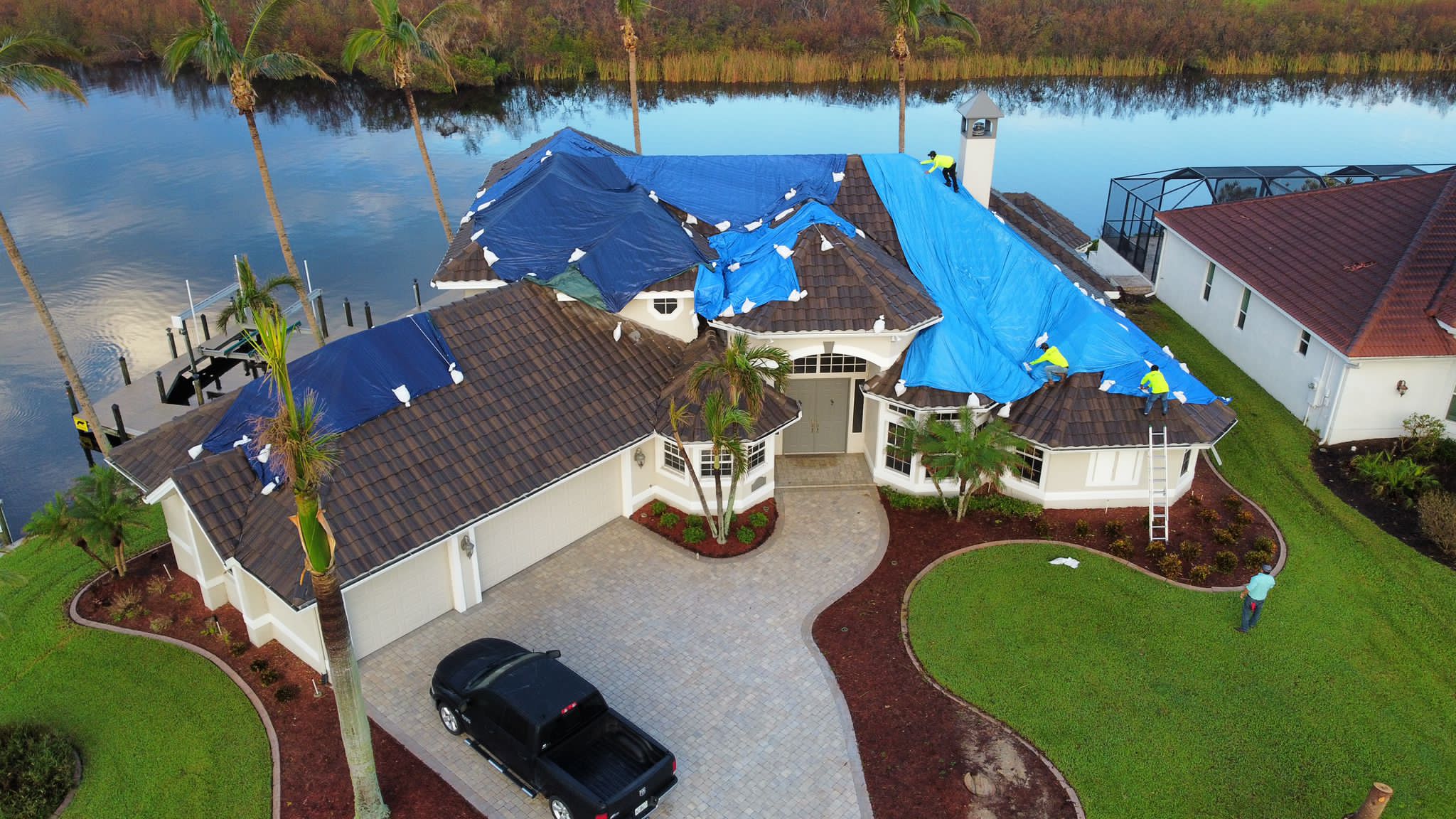 Waterfront home with its tile roof covered in blue tarps before RoofWrap